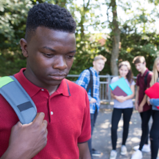 Een groep jongeren met lichte huidskleur lacht om een jongen met donkere huidskleur