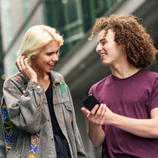 Een meisje met lichte huidskleur en jongen met getinte huidskleur bekijken iets op de telefoon van de jongen.